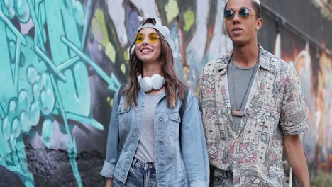 hipster couple in stylish clothes in love talking and walking down the street near a graffity wall