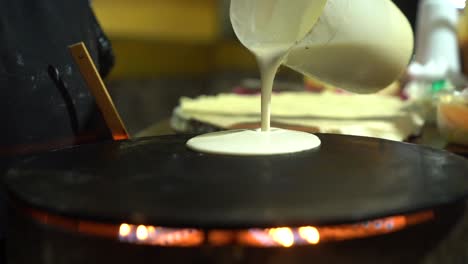 cook pouring and spreading crepe batter across metal griddle on a mexican street market