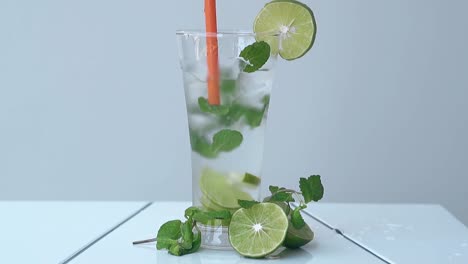 La-Paja-De-Naranja-Revuelve-El-Cóctel-Mojito-Frío-Sobre-Una-Mesa-Blanca.