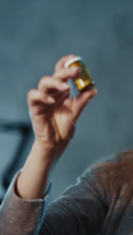 pensive blonde woman patient looks at new remedy in small bottle prescribed by doctor spending time in semi-dark room at home extreme close view slow motion