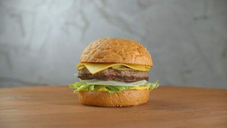 Una-Hamburguesa-En-Una-Tabla-Con-Papas-Fritas-Esparcidas.-Primer-Plano-De-Una-Deliciosa-Hamburguesa-Casera-Fresca-Con-Lechuga,-Queso,-Cebolla-Y-Tomate-Sobre-Una-Tabla-De-Madera-Rústica-Sobre-Un-Fondo-Oscuro