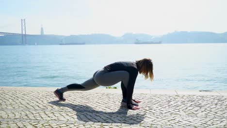 mujer joven deportiva estirándose cerca del río