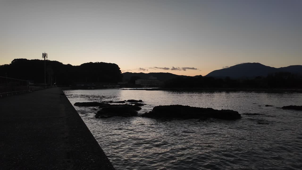 Dark silhouettes of hills and rocks encircling Nachi Bay, creating a stunning backdrop during the tranquil golden hour of sunset