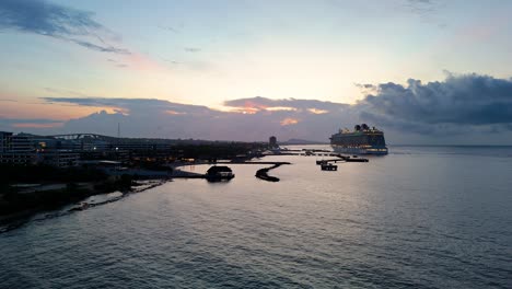 drone rises from beach as large cruise ship docked at port lights up at blue hour in the caribbean