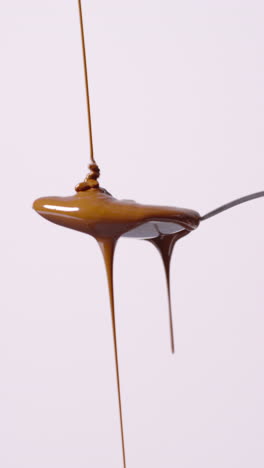 video vertical de chocolate derretido que se vierte en una cuchara y se desborda contra un fondo blanco con espacio de copia 1