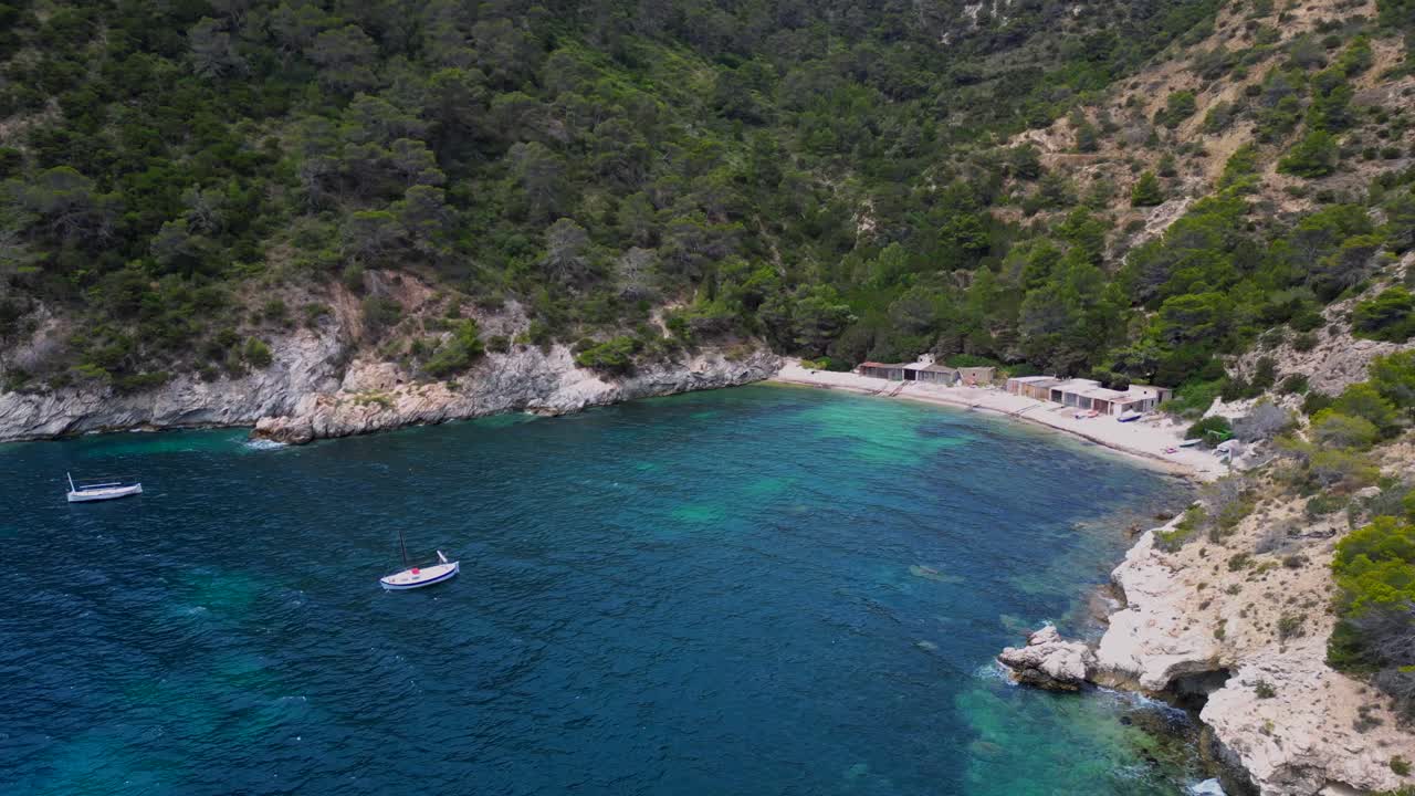 Cala Llentrisca beach with turquoise water and Barques de pescadors Huts in Ibiza, Spain, in summer. Smooth aerial view flight panorama overview drone