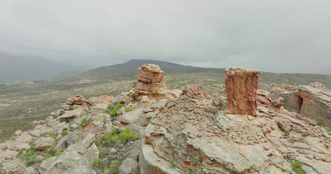 Drone berputar mengelilingi formasi batuan di lanskap gurun Kawasan Alam Liar Cederberg di Afrika Selatan - pegunungan di balik awan terlihat di latar belakang