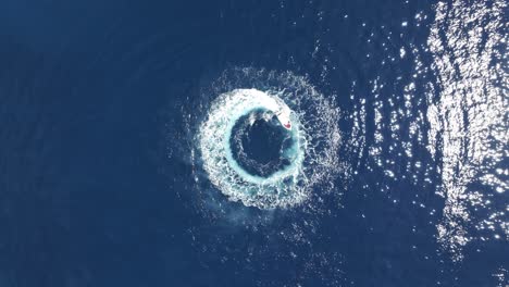 drone shot of boast spinning in circles in blue sea water, top down aerial view 50fps