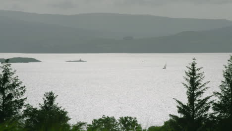 FOCUS-PULL-to-a-sailing-boat-on-a-glistening-Sound-of-Mull,-the-island-of-Mull-behind