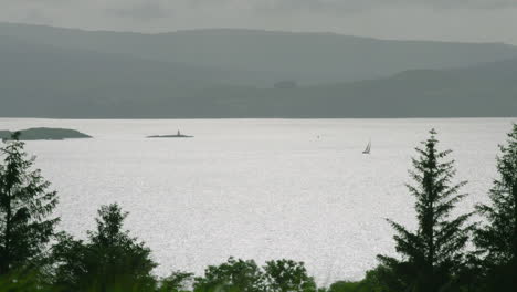 focus pull to a sailing boat on a glistening sound of mull, the island of mull behind