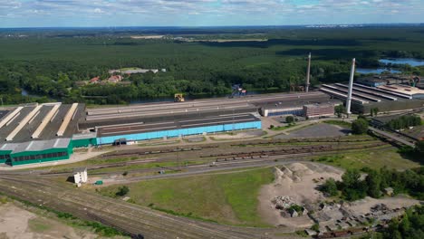 Hennigsdorf steel factory with chimneys, warehouses, railway, near river and forest in summer. Great aerial view flight wide orbit overview drone