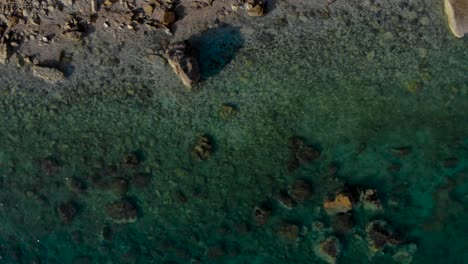 Acantilados-Y-Guijarros-Bajo-El-Agua-De-Mar-Turquesa-En-Una-Playa-Remota-En-La-Costa-Mediterránea