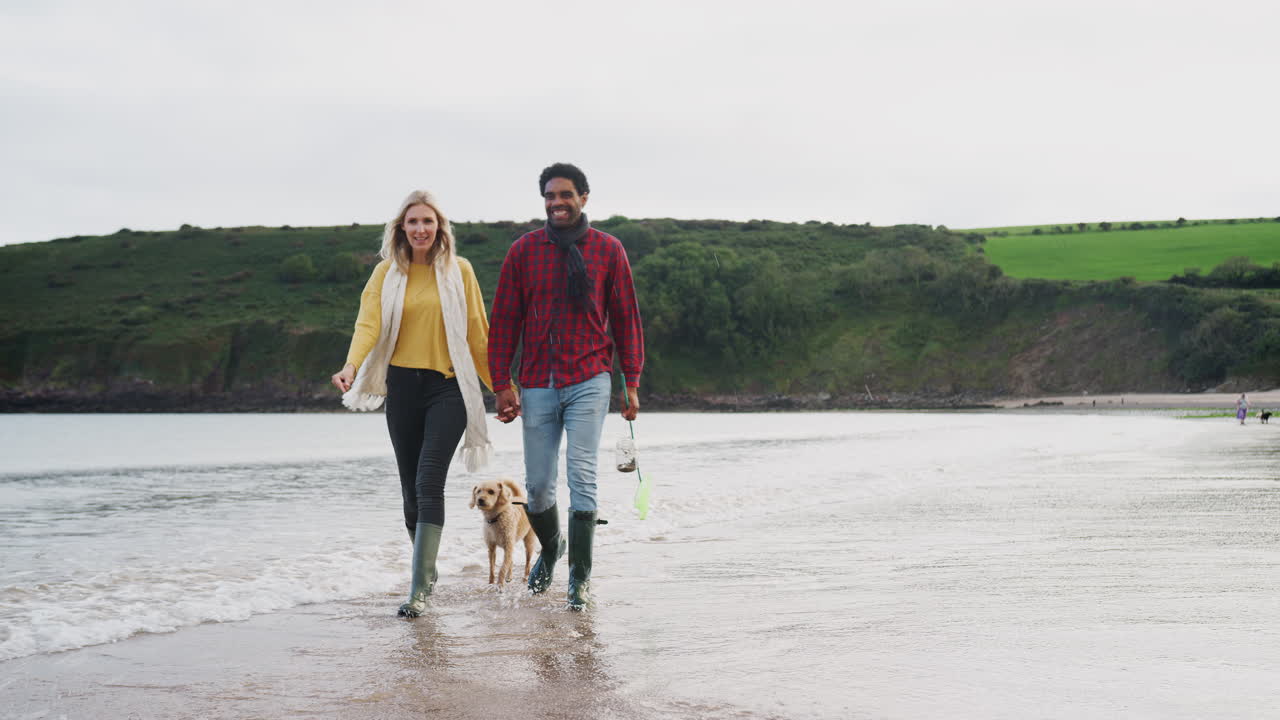 familia multicultural con perro de compañía caminando a lo largo de la costa de la playa en vacaciones de invierno