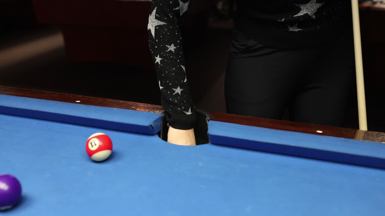 Een persoon haalt een biljartbal uit een pocket van een pooltafel