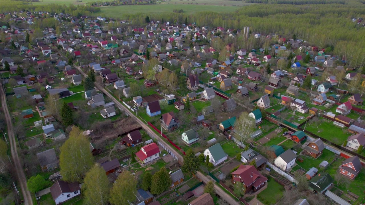 Lav luftudsigt bevæger sig over landsbyhuse med farverige tage, haver, veje og grøn skov til landlig boliglivsstil, rejser på landet og ejendomstemaer