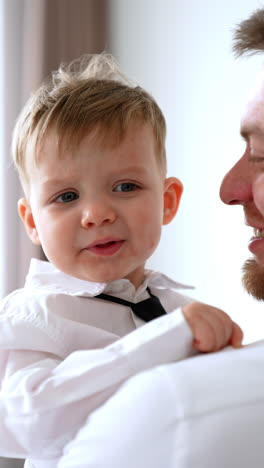 adorable baby boy in white shirt and black tie is in dad's hands. father and son concept. vertical video.