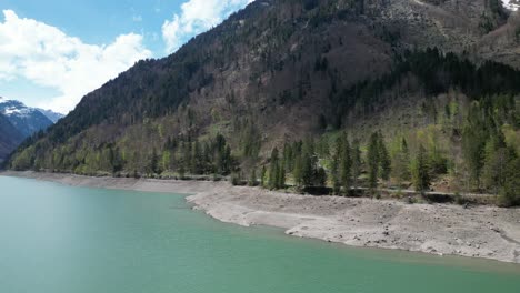 aerial forward view of shoreline of an alpine lake in a fantastic mountain landscape