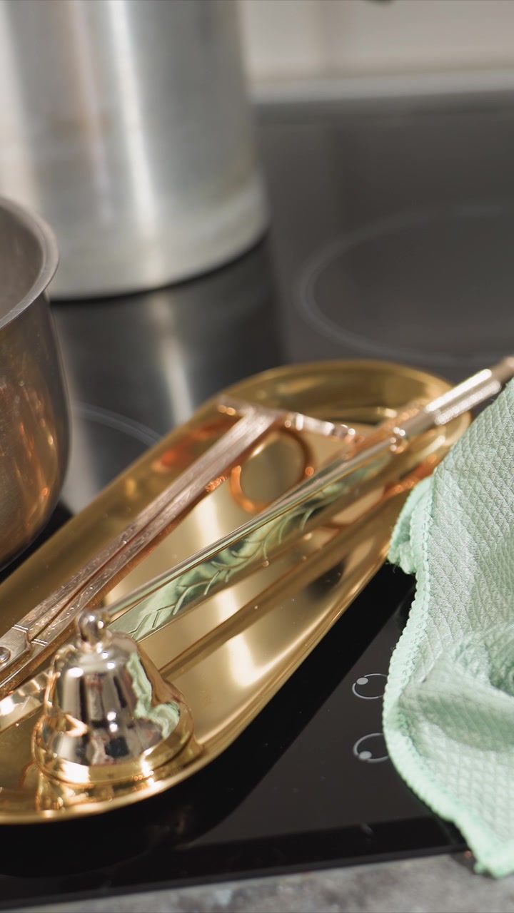 Close up of gold tray holding kitchen utensils on induction cooktop with pots in background. scene features soft lighting and detailed textures including metallic reflections and smooth