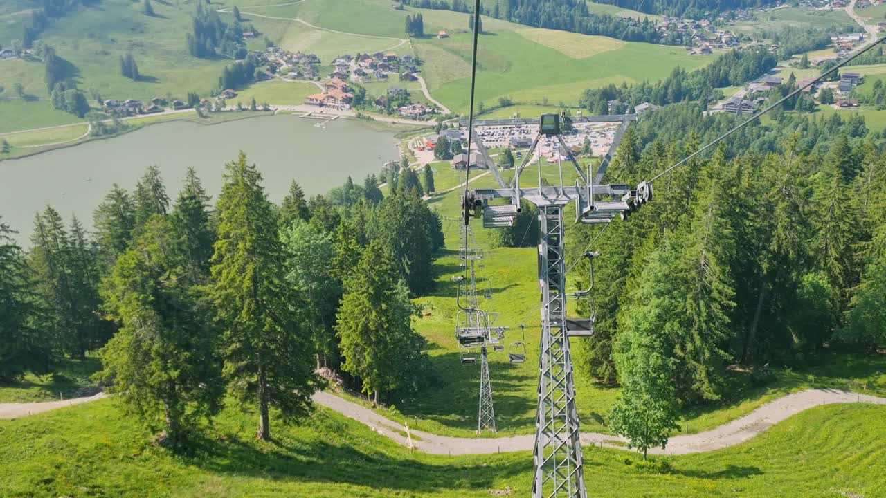 Vista da una lenta seggiovia che scende verso il lago Schwarzsee e alcune case sparse, catturando il fascino alpino di Plaffeien, Friburgo, Svizzera, in una soleggiata giornata di primavera