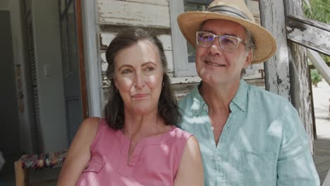 happy senior caucasian couple talking and embracing on porch of wooden beach house, in slow motion