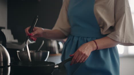 pretty woman in blue apron is frying pancakes in morning cooking breakfast for family housewife is turning pancake