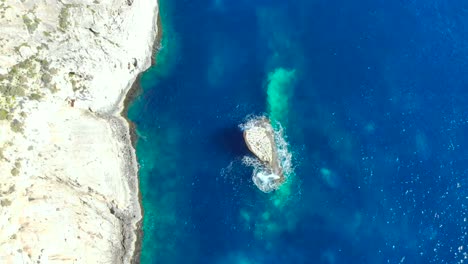 drone shot over rocks and cliffs with wave hitting a small rock in the mediterranean sea of malta 3