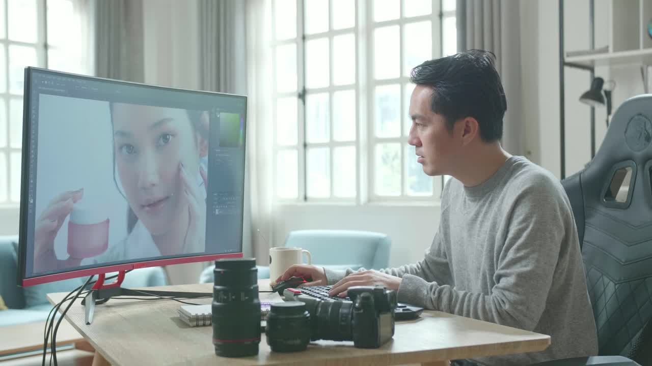 アジアのカメラマンが長袖のtシャツを着て自宅で働いている間デスクトップコンピュータを使って写真を編集しています