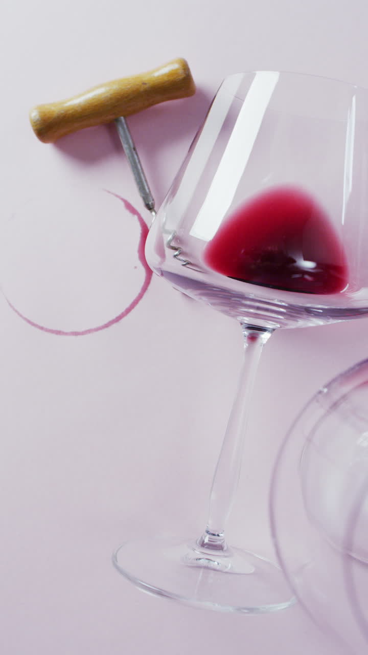 Video verticale di bicchieri di vino rosso, cavatappi e macchia di vino su superficie bianca