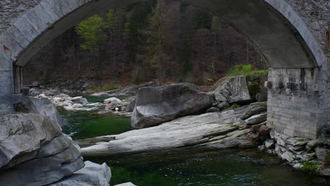 Aerial-view-of-historical-bridge-and-stream-in-Verzasca-valley,-Switzerland