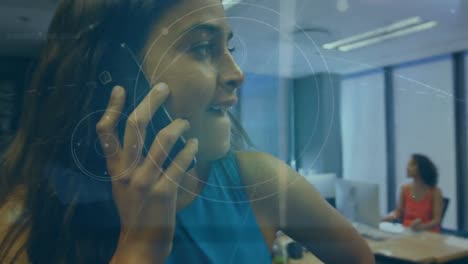 Animation-of-shapes-over-biracial-businesswoman-talking-on-smartphone-in-office