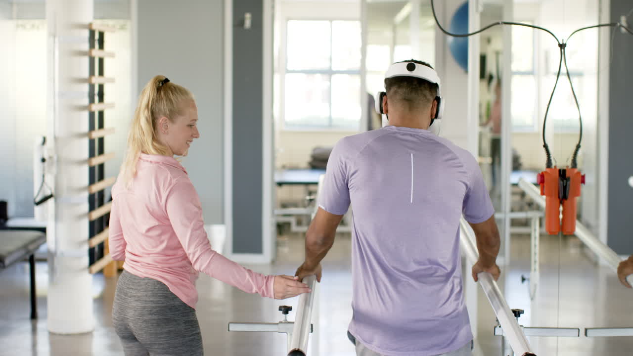 Man in prosthetic leg walking using VR headset with therapist on parallel bars