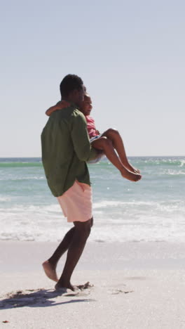 sonriente padre afroamericano con la hija llevando en la playa soleada
