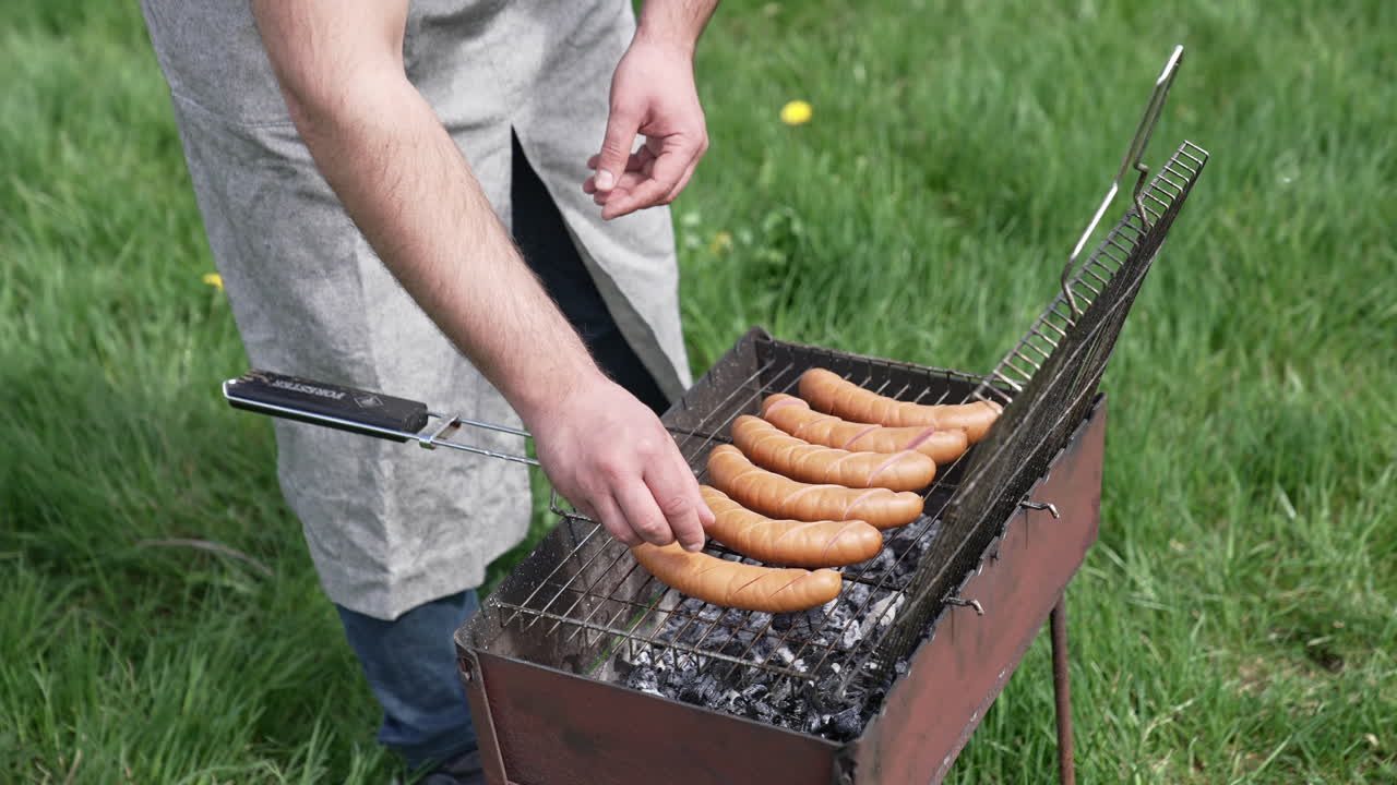 Man hands grilling tasty sausages on barbeque. Delicious grilled meal on fire.