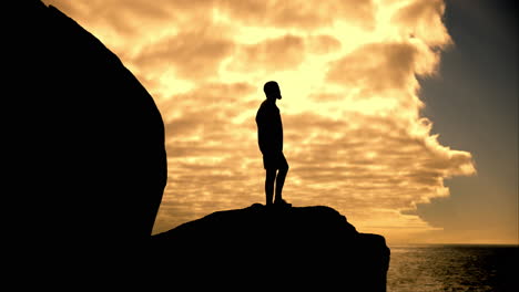 silhouette of a man standing on a cliff at sunset