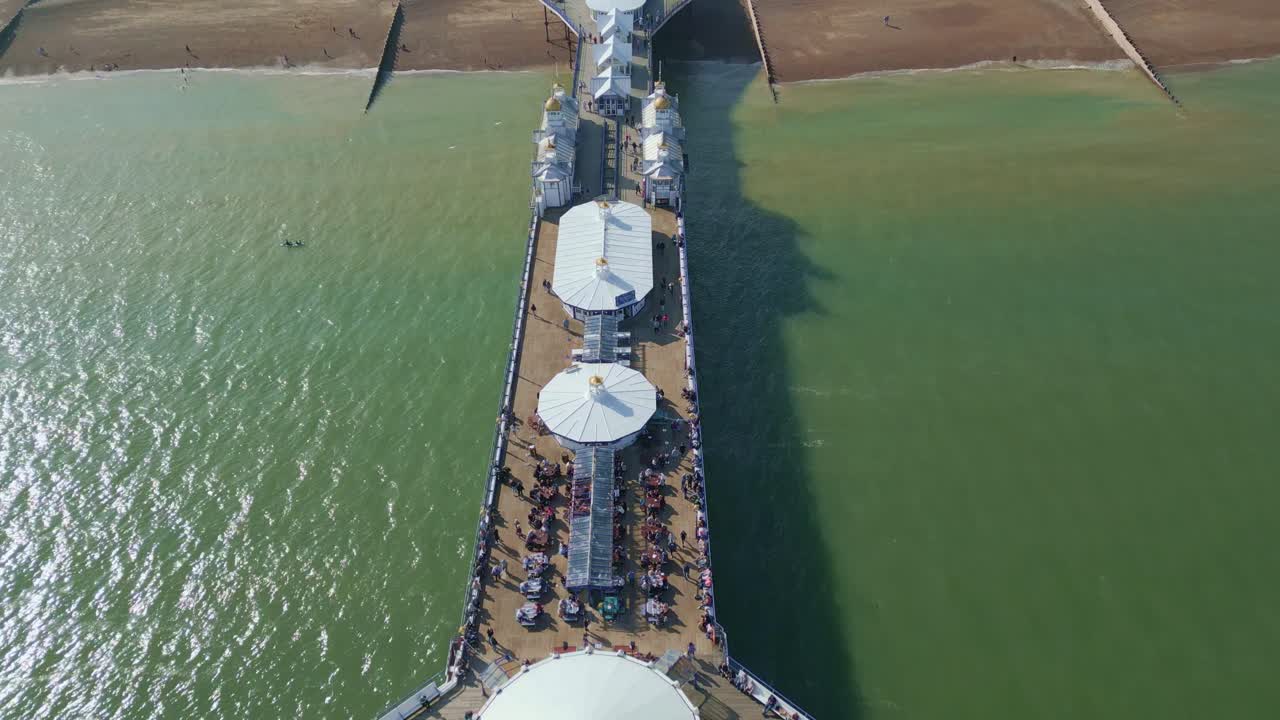 걸어다니는 사람들과 함께 이스트본 피어 위와 위를 날고 있습니다.