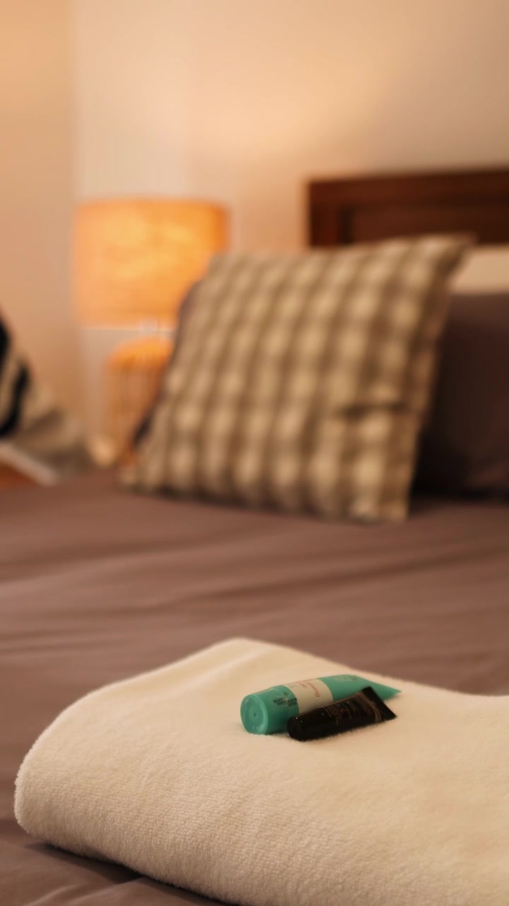 A bedside lamp illuminates a cozy bedroom, enhancing the warm ambiance with soft lighting and neatly arranged bedding