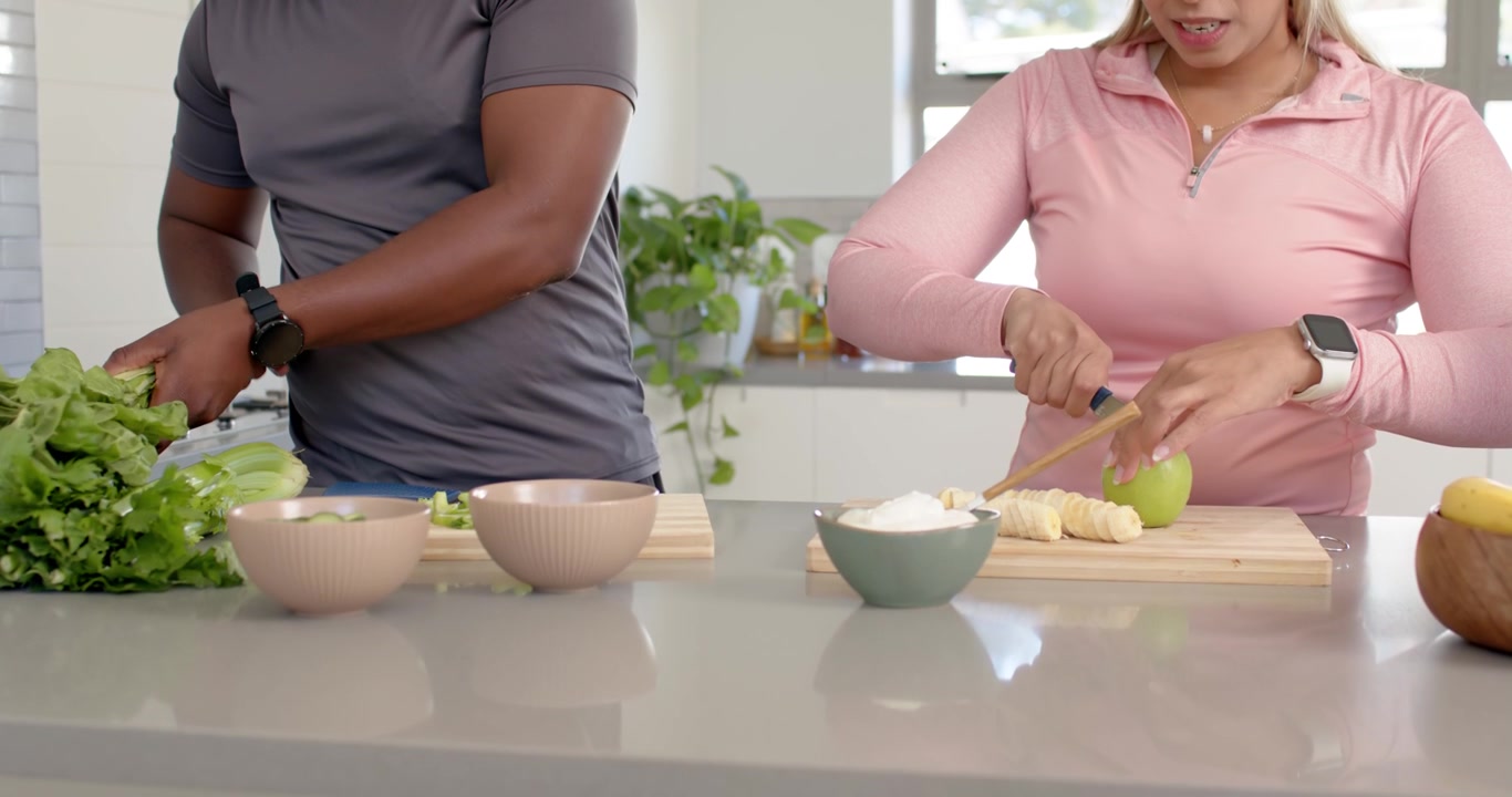 Coppia afroamericana che solleva un coperchio e taglia la frutta, tritando la lattuga sull'isola della cucina per servire.