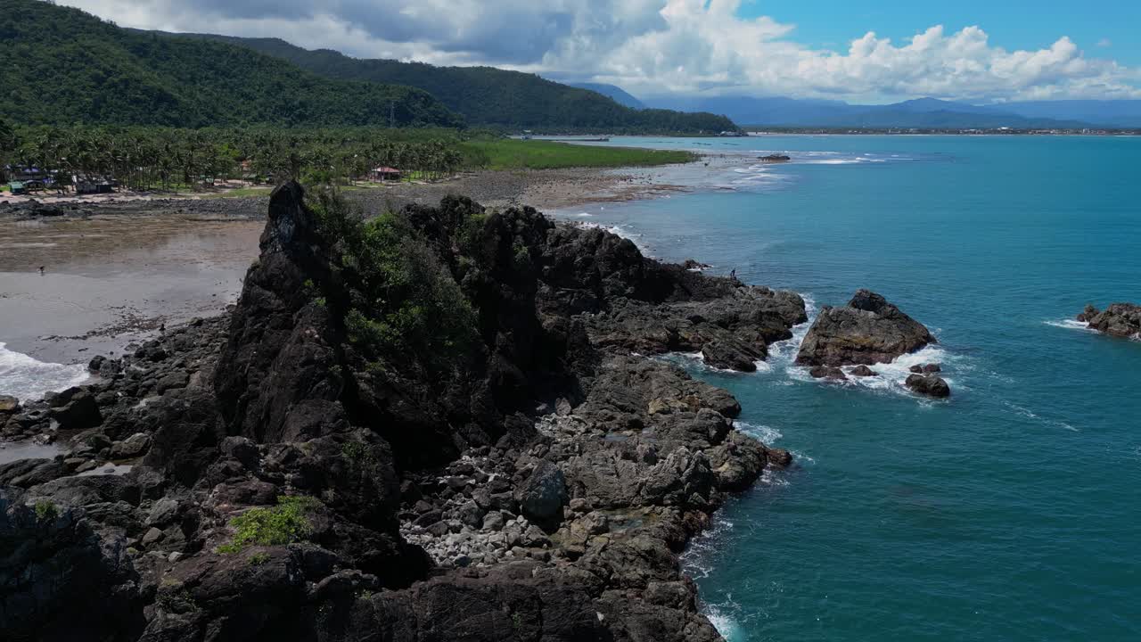A smooth dolly-out drone shot gradually retreats from the small rocky mountains along the shore, revealing the full stretch of the coastline and the vast ocean beyond.