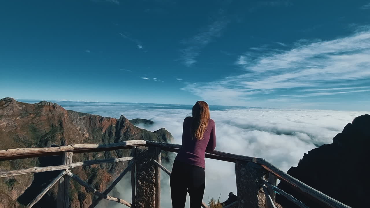 Woman tourist admiring a stunning mountain view above the clouds from a viewpoint in Madeira, Portugal