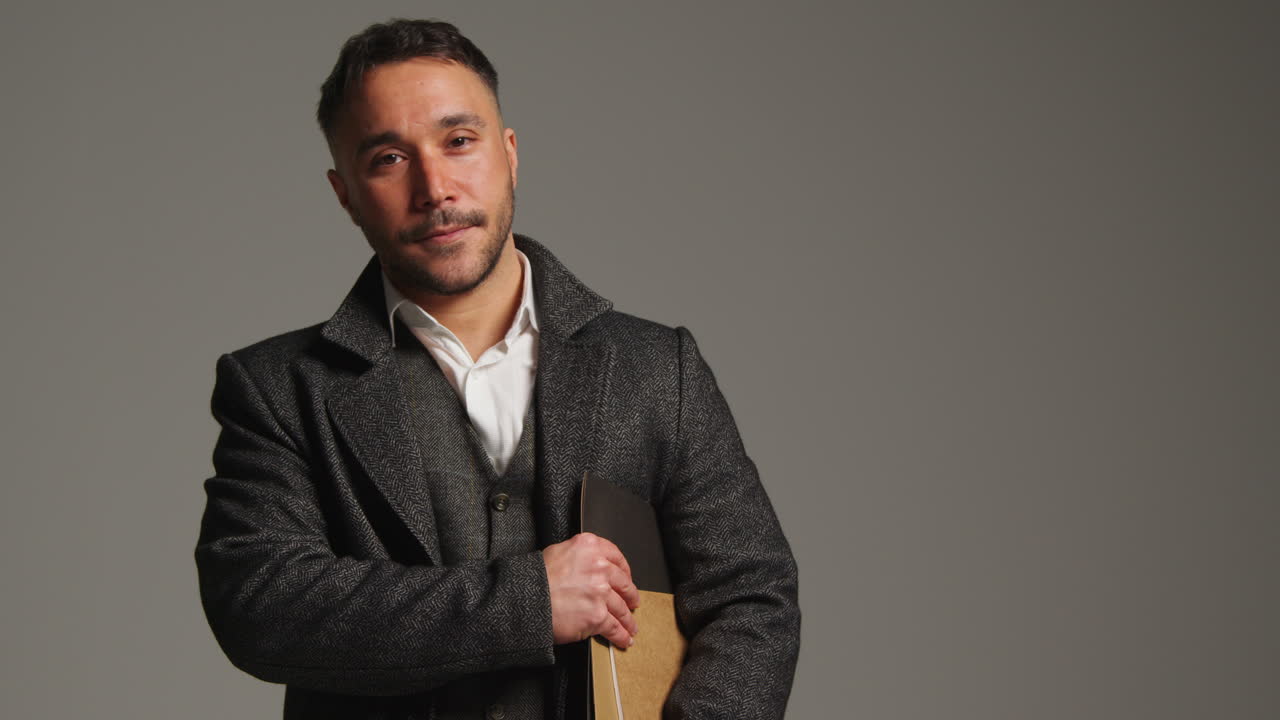 웃는 성숙한 남성 교사 또는 사업가의 스튜디오 초상화, 그의 팔 에 폴더와 함께 회색 배경에 서 있습니다.