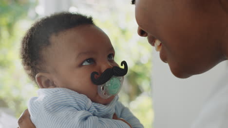 funny baby with moustache pacifier happy mother having fun with toddler at home enjoying silly humor with child sucking on dummy