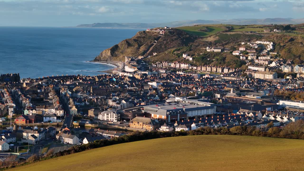 Stunning drone footage of Aberystwyth from Pen Dinas Hill, capturing the entire town, coastline, and sunset in golden hour light on a beautiful evening.