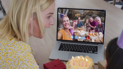 caucasian mother and daughter sitting at table using laptop having birthday video call