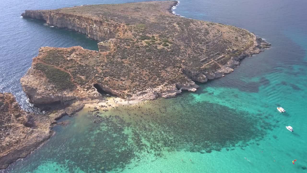 Blue Lagoon, a popular tourist holiday destination in Malta seen from the air. Warm clear water draws people to swim and snorkel in the turquoise Mediterranean Sea.  Flying backwards, ZOOM OUT.