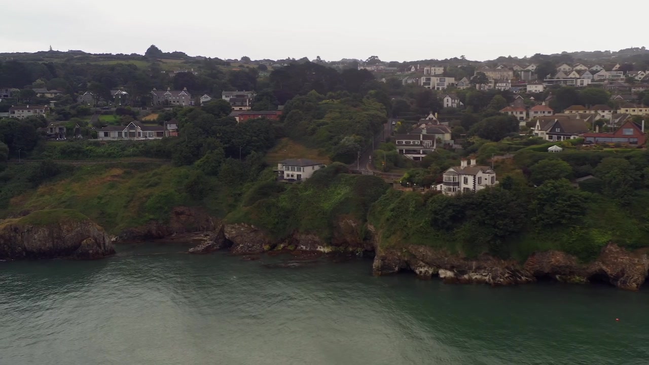 Panorâmica aérea em movimento ao longo de uma comunidade costeira idílica em Howth, Norte de Dublin, Irlanda, em um dia nublado