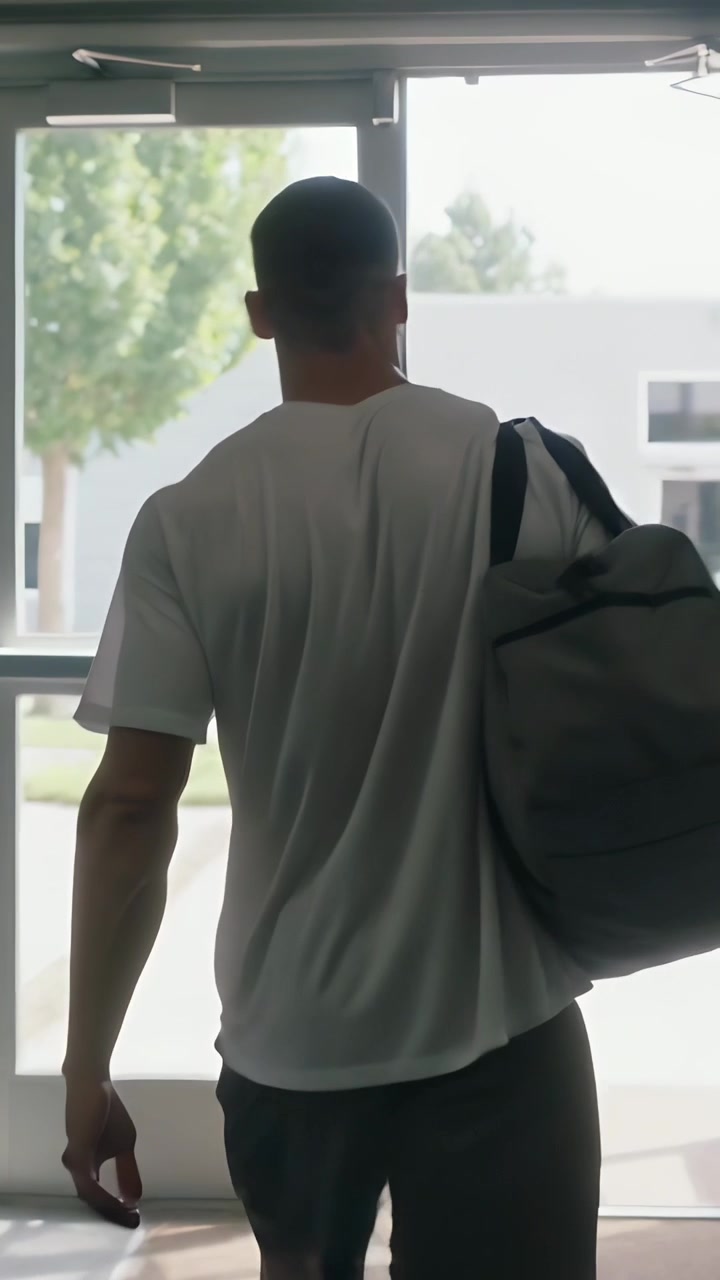 Vertical video: Walking man in gym clothes with gray duffel toward gym exit post-workout