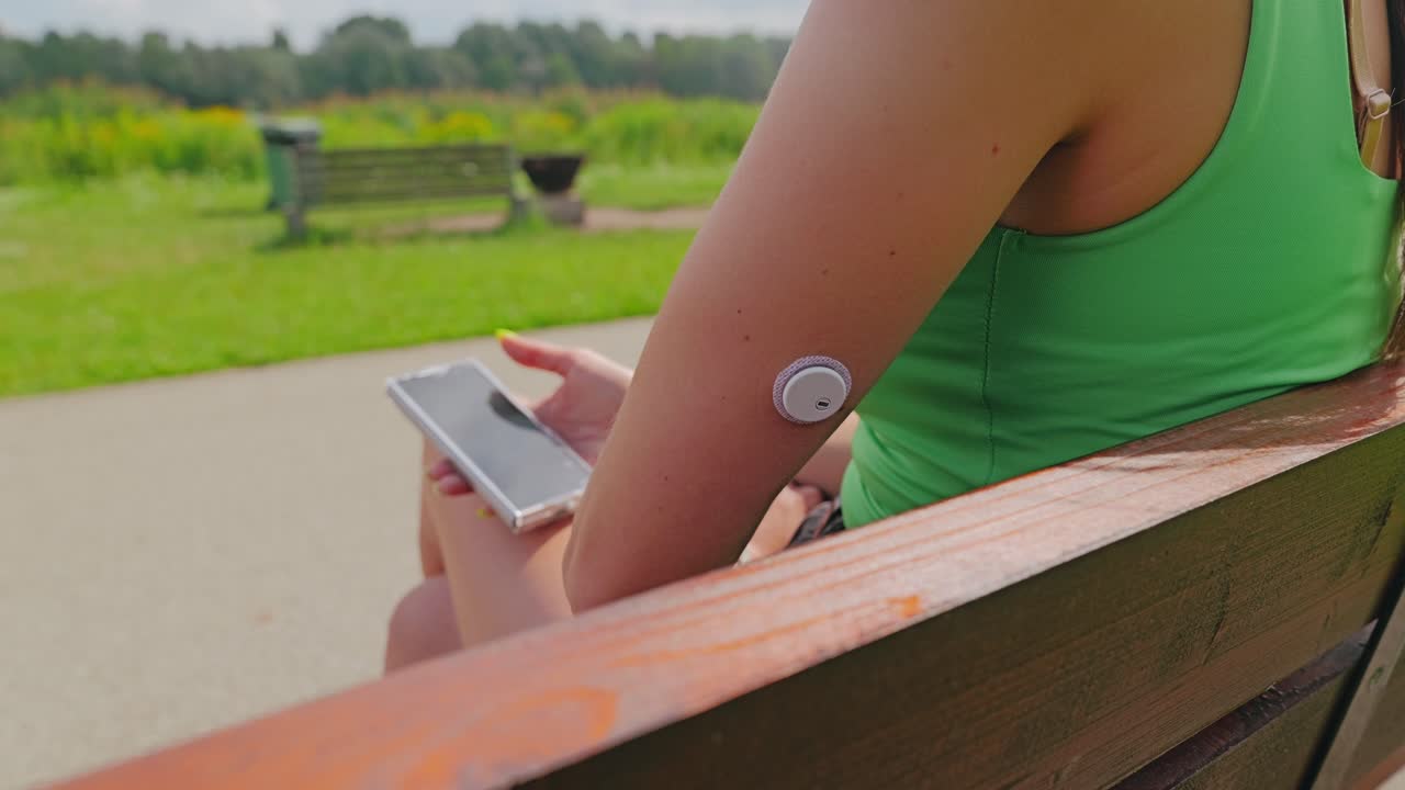Woman using glucose monitoring sensor and phone app outdoors in daylight