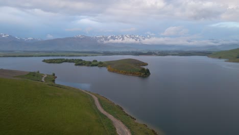 drone footage of a tiny island on lake opuha at the foothills of new zealand's southern alps