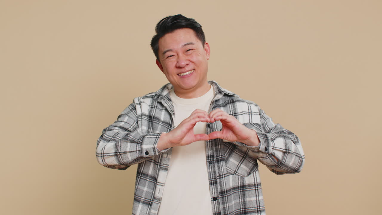 Happy asian man makes heart gesture demonstrates love sign expresses good feelings and sympathy