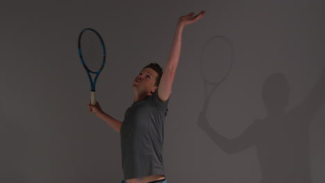 studio shot of male tennis player serving in match hitting ball with racket against grey background 2